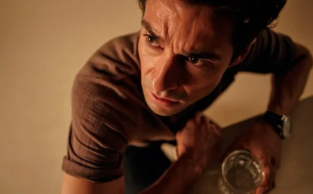 Мужчина сидит за столом со стаканом в руке